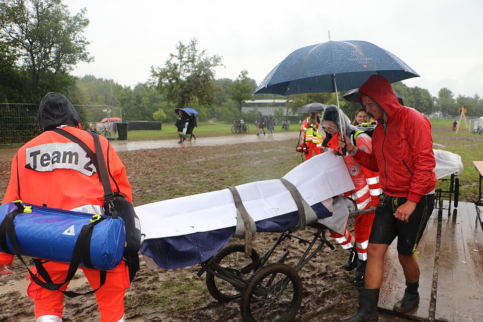 „Ein Patient wird im strömenden Regen vom Festivalgelände abtransportiert (Foto: Eisenmann P., BRK Kreisverband Freising)“